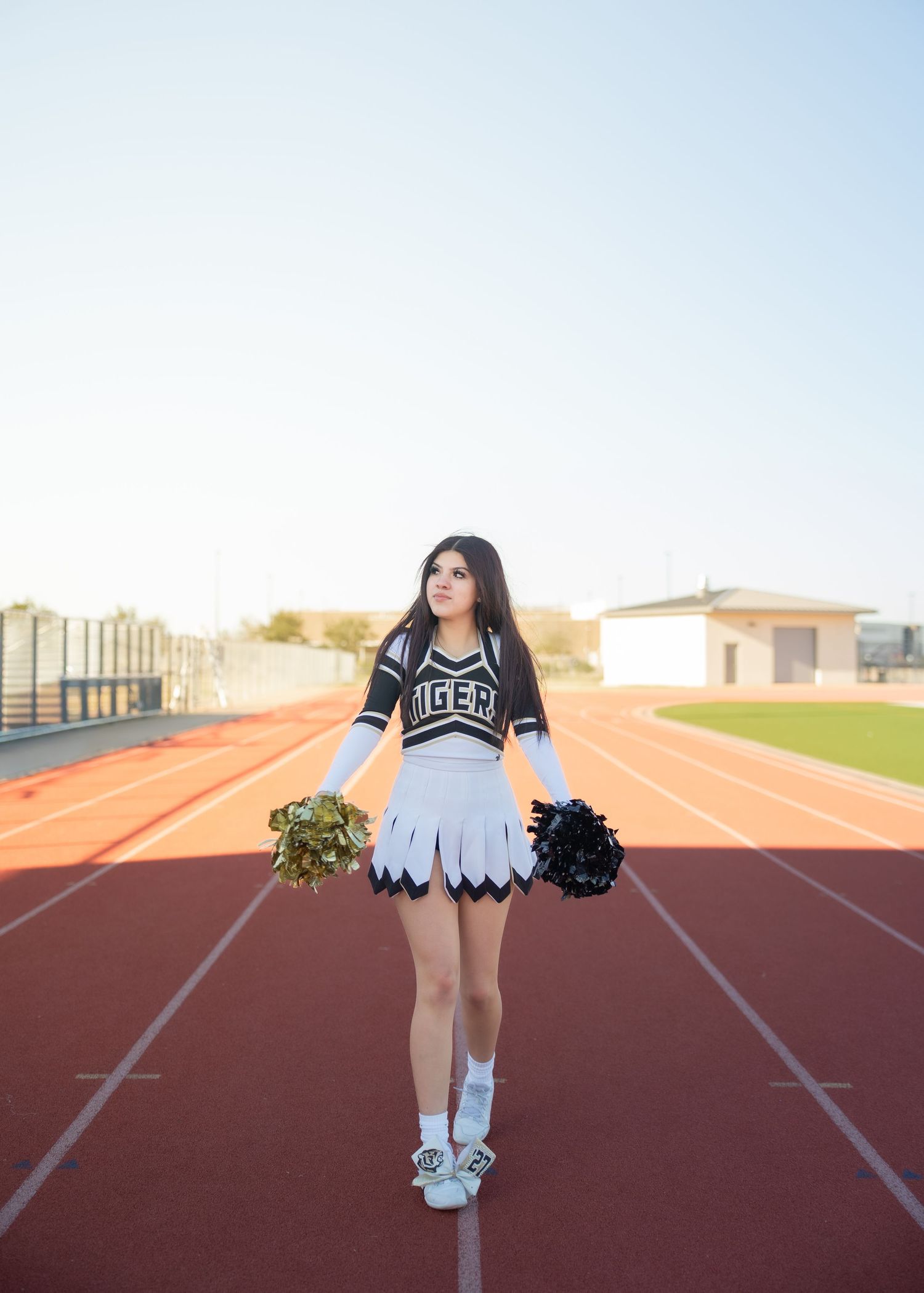 CyPark High cheerleader posing on football field with pom-poms, smiling in uniform