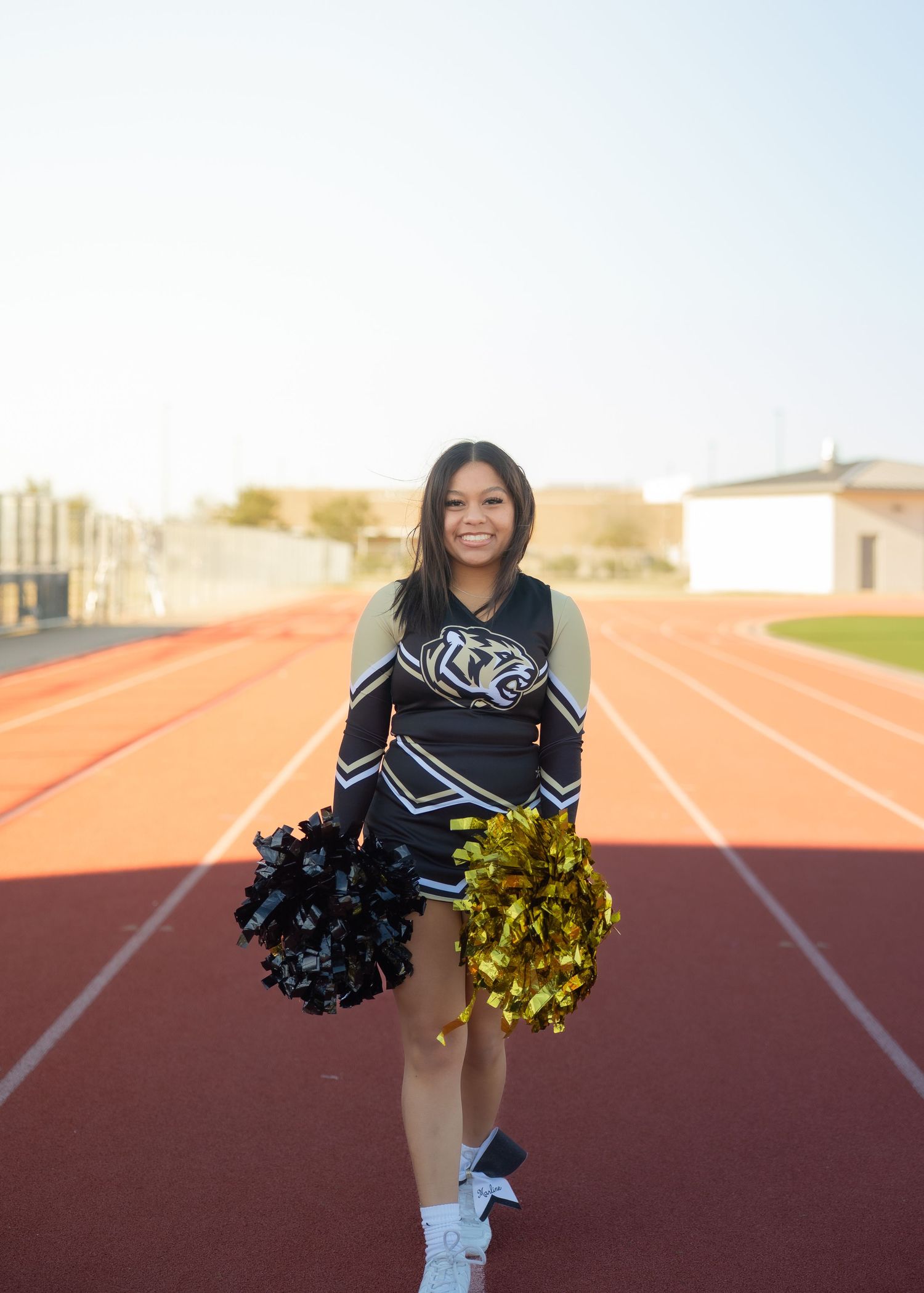 CyPark High cheerleader posing on football field with pom-poms, smiling in uniform