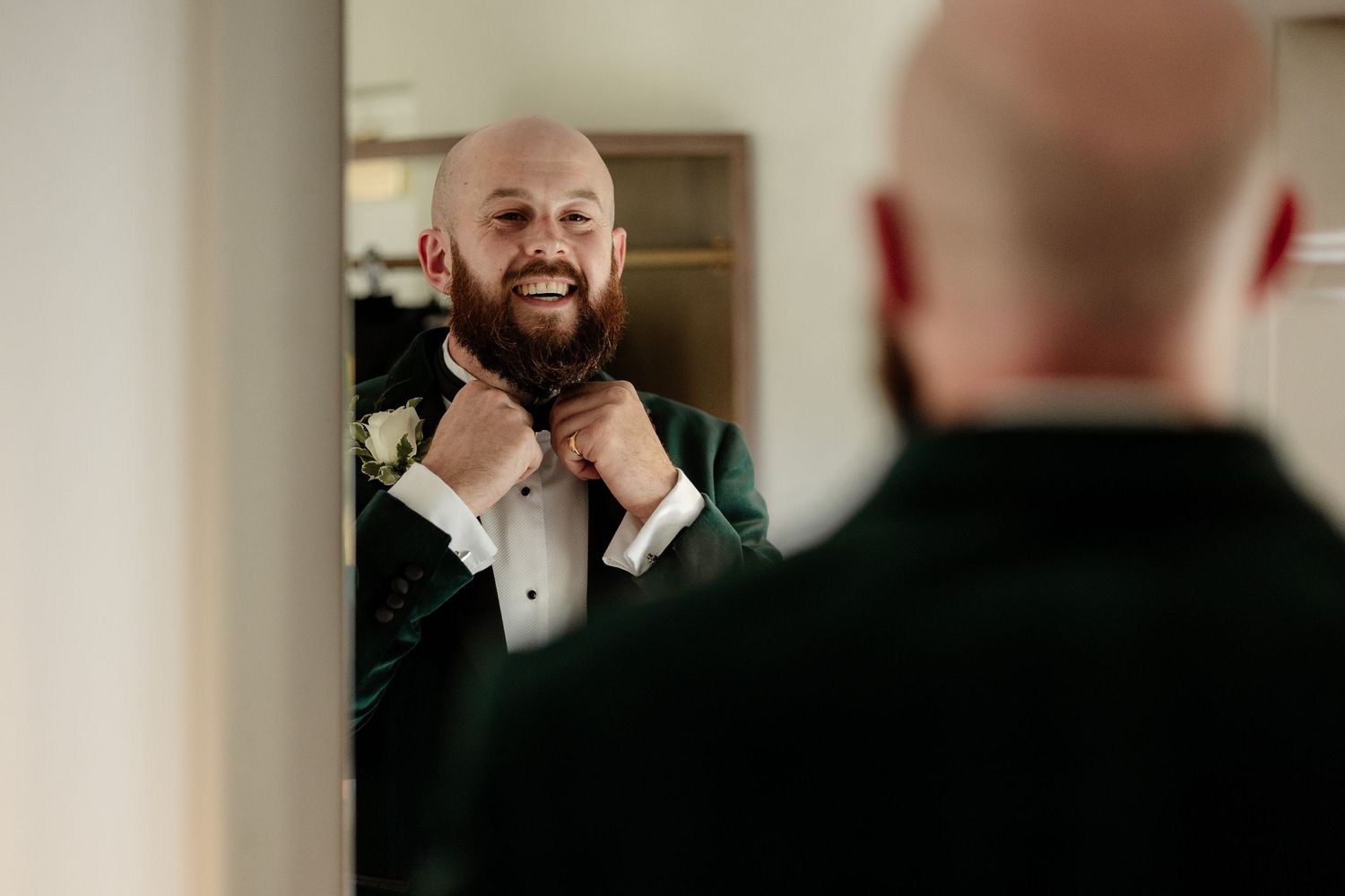 A joyful wedding celebration scene with people adjusting formal attire and laughing together in a bright indoor setting.
