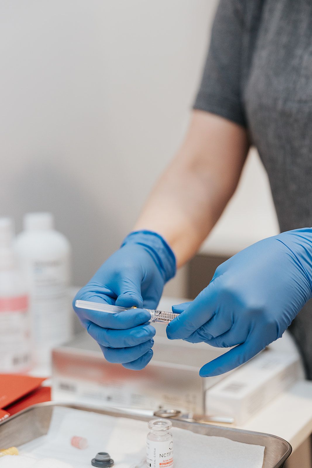 Hands wearing blue medical gloves prepare samples on a laboratory work surface with testing materials.