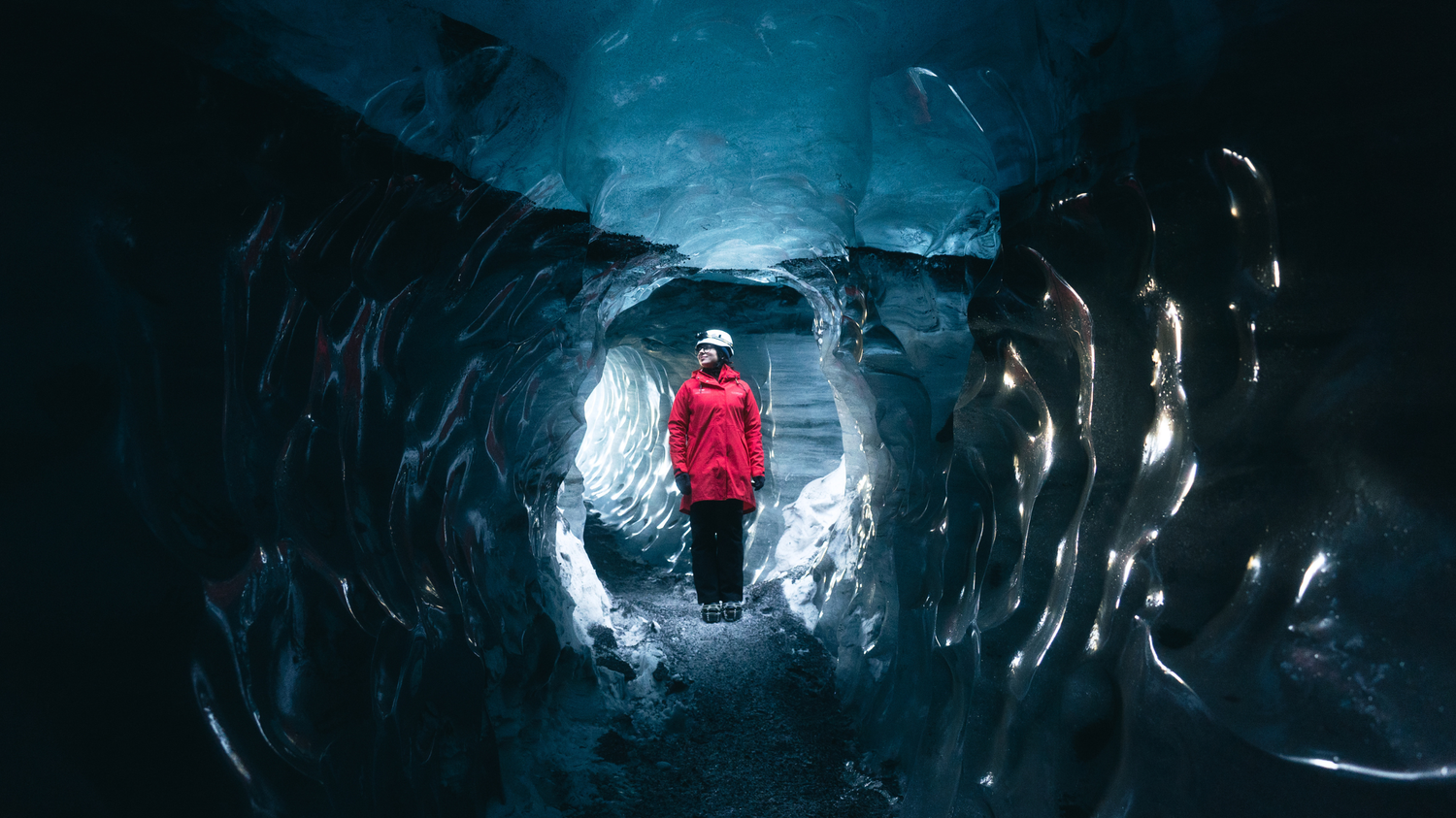 Person in red attire standing inside the blue Katla ice cave in Iceland