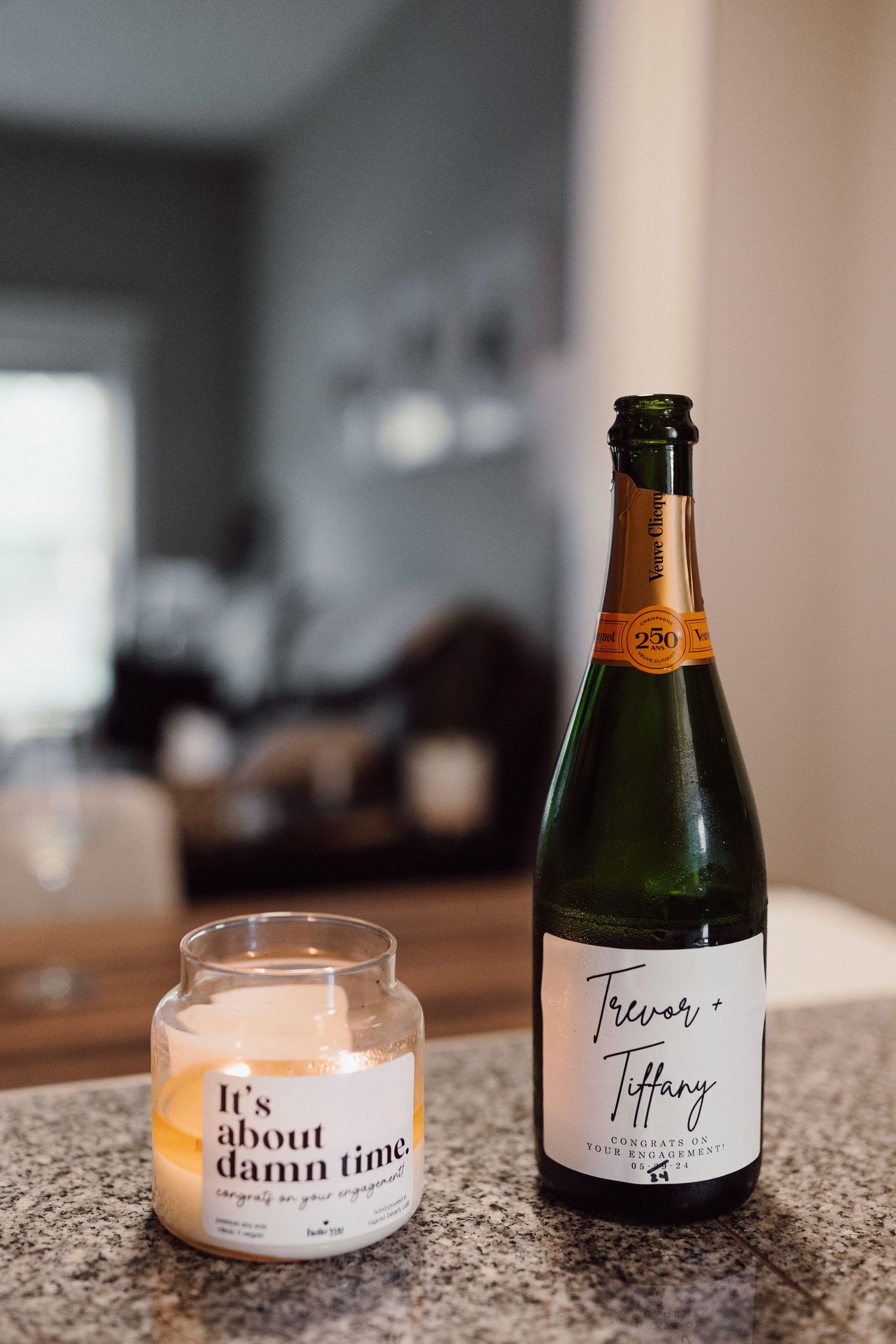 Champagne bottle and candle with 'It's about damn time' text on granite countertop in moody lighting.