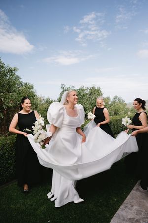 Wedding party helps adjust a flowing white wedding dress outdoors.