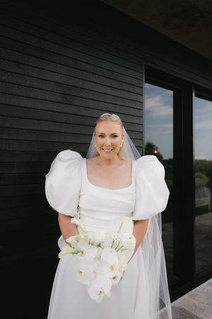 Elegant bride in puff sleeve wedding dress holding white orchid bouquet.