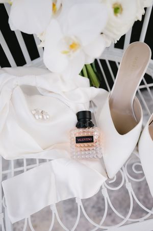 White bridal accessories including shoes and perfume arranged on an ornate white surface.