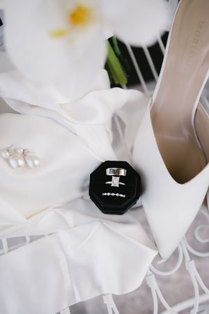 Wedding details featuring a white stiletto heel and engagement ring on delicate white fabric.