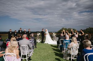 Outdoor wedding ceremony on a grassy hilltop with white chairs and scenic views.
