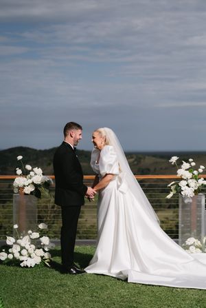 Wedding couple shares intimate moments on a grassy hilltop decorated with white floral arrangements.