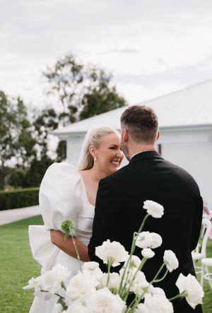 Elegant wedding couple poses among white flowers on a grassy hillside.