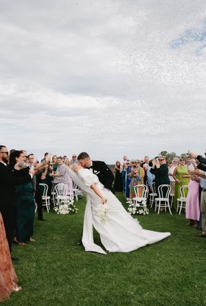Wedding celebration on lawn with guests throwing confetti as couple shares romantic moment.