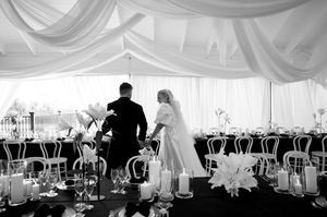 Black and white photo of couple entering decorated reception tent with elegant table settings.
