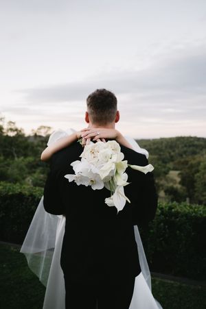 White floral bouquet adorns a formal black suit against a sunset backdrop.