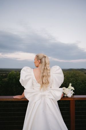 Back view of wedding dress with dramatic puff sleeves against scenic landscape.