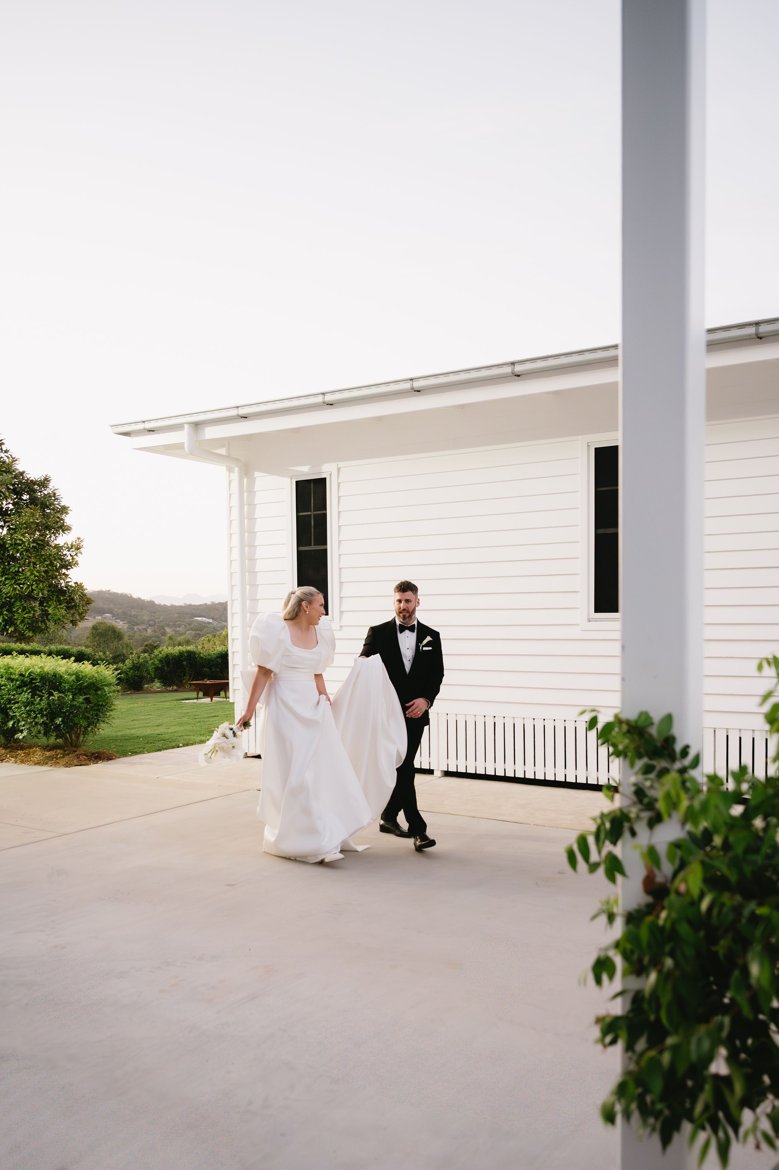 Elegant couple walking outside white chapel building during wedding celebration.