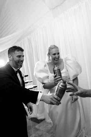 Wedding guests share champagne toasts under a white tent during reception celebrations.