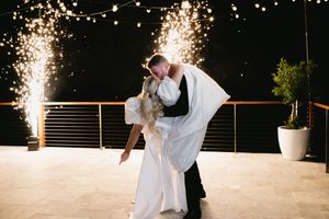 A couple in formal wedding attire dances together under sparkler fireworks at an outdoor evening reception.