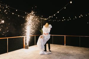 Wedding couple dances under twinkling string lights and sparklers at an outdoor evening reception.