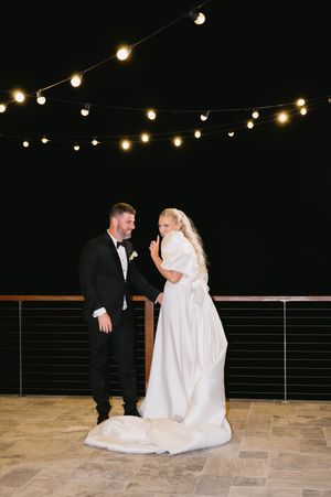 A couple shares a romantic moment on a patio under string lights at night during their wedding celebration.