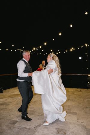 A couple dances on an outdoor patio under twinkling string lights at night during their wedding celebration.