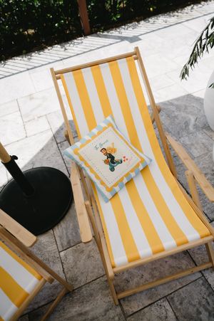 Yellow and white striped beach chair with decorative throw pillow on outdoor patio.