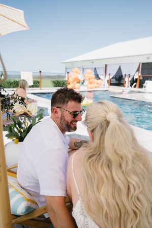 Wedding celebration by a poolside with white sun shades and orange balloon decorations.