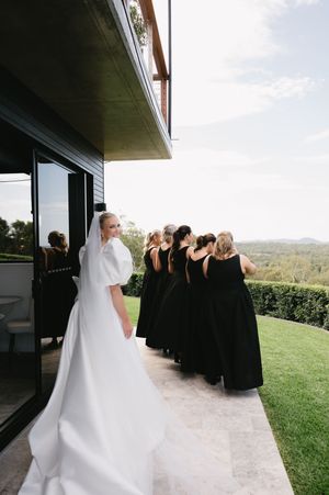Wedding party in black dresses standing on outdoor terrace with scenic view.