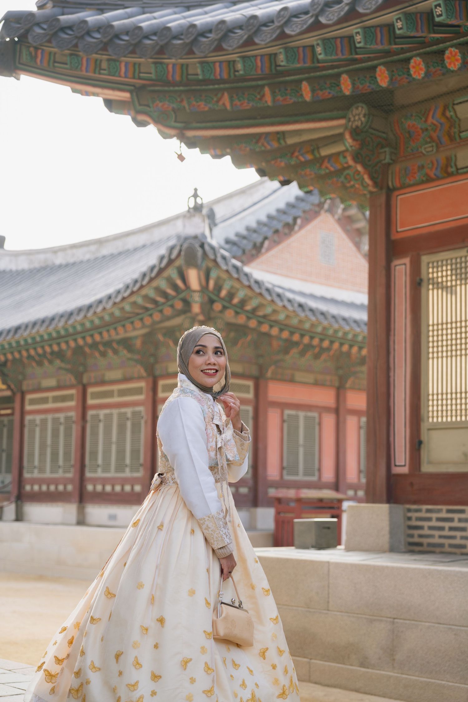 A figure in a white hanbok dress poses gracefully against traditional Korean palace architecture with ornate rooftops.