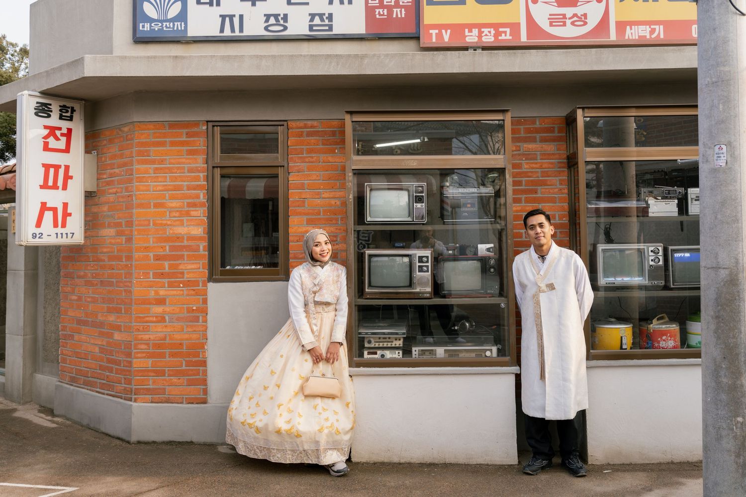 Panoramic view of a Korean storefront with brick walls and multiple business signs in both Korean and English text.