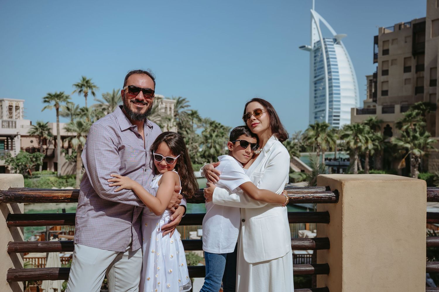 A family poses together outdoors in Dubai with the iconic Burj Al Arab hotel visible in the background.