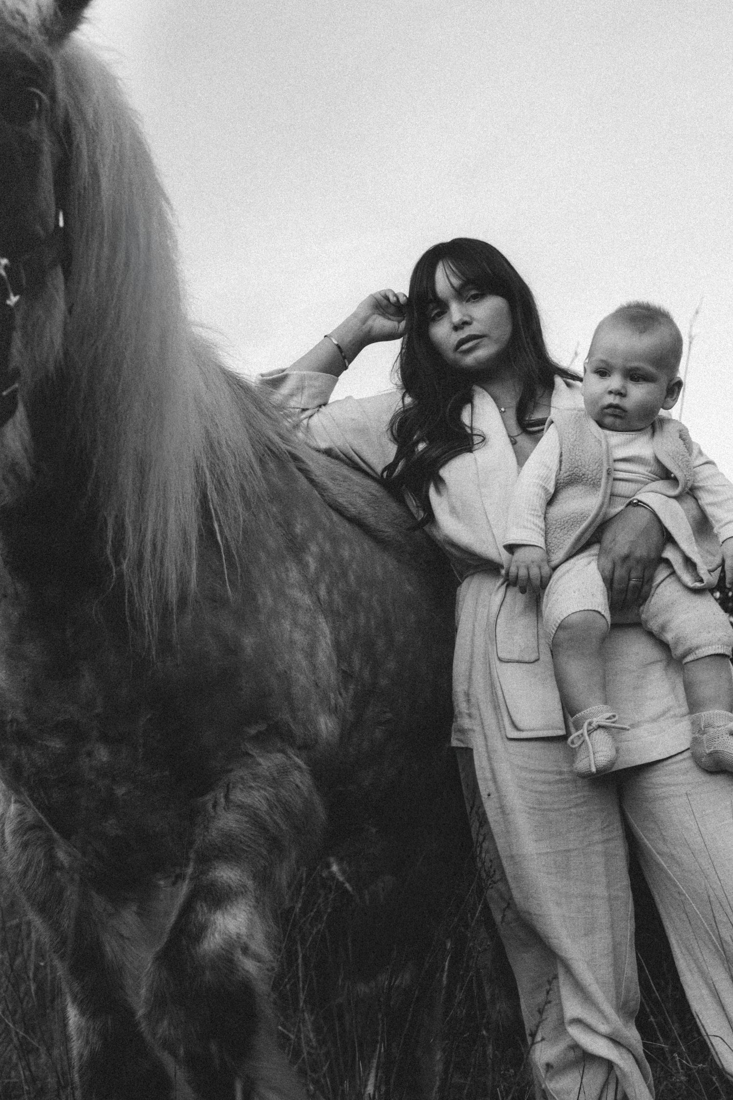 A sequence of black and white photos showing a mother and child in light colored clothing being lifted onto a dark horse. Javea photographer