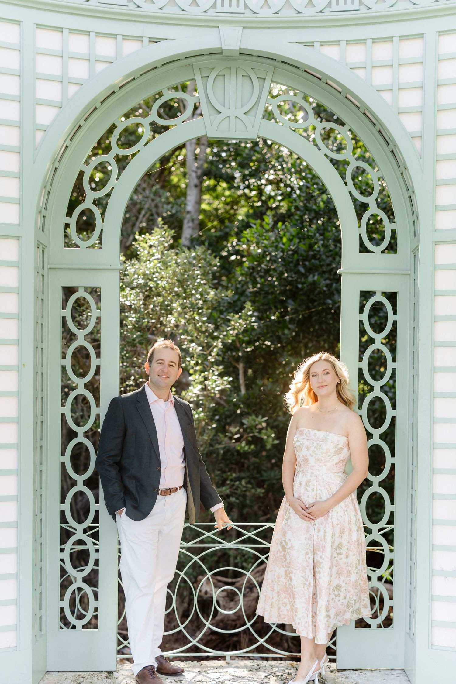 Elegant mint green gazebo with ornate lattice work frames a couple in formal wear.