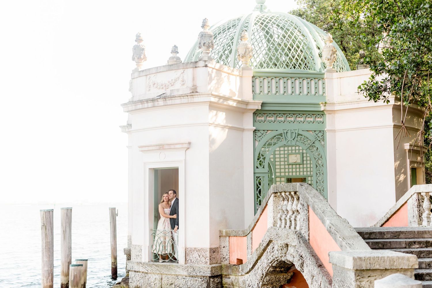 Elegant white stone pavilion with mint green dome overlooking water at Vizcaya Gardens in Miami.