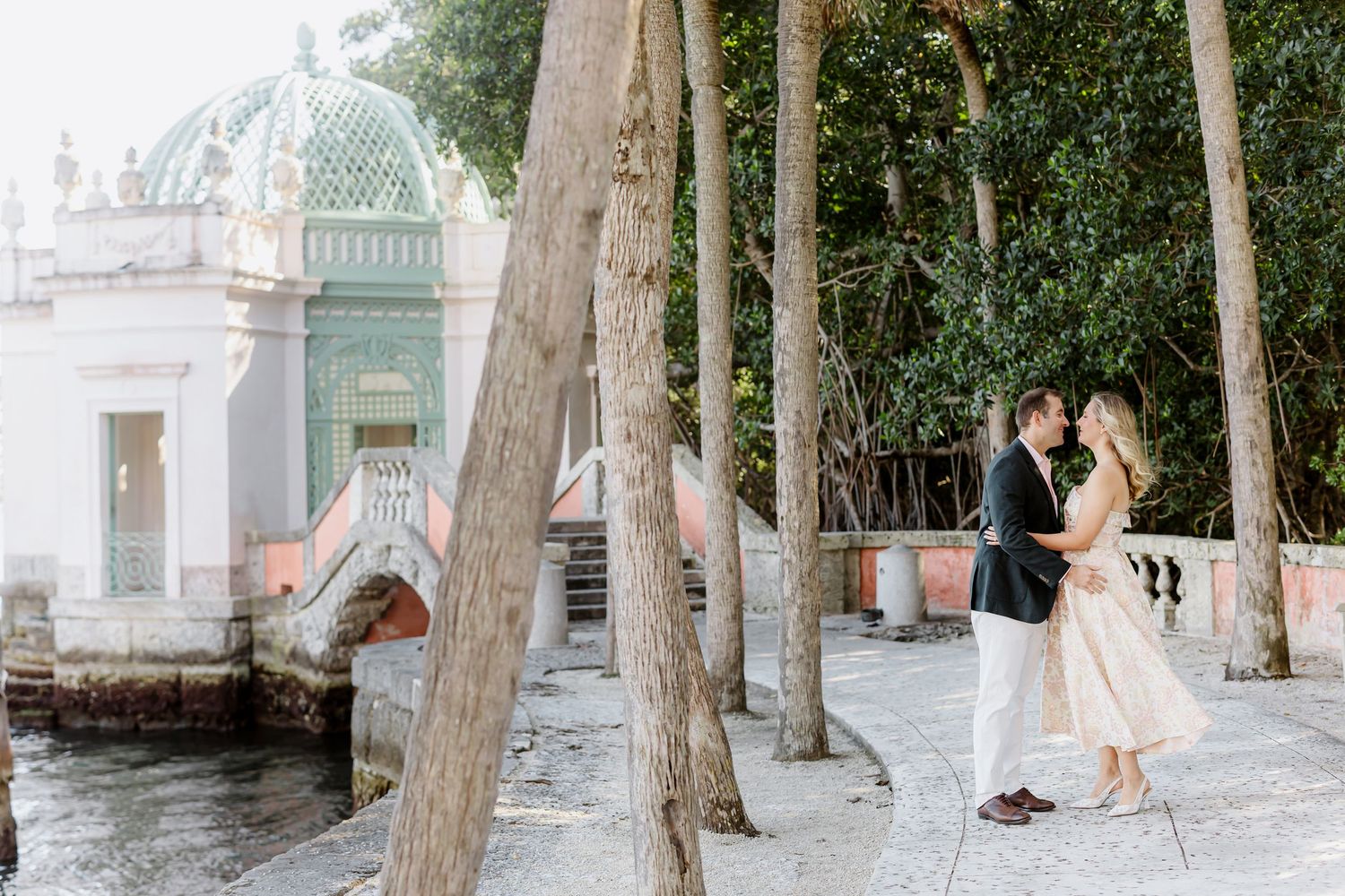Romantic couple stands on a waterfront promenade near ornate white architecture with mint green dome in Miami.
