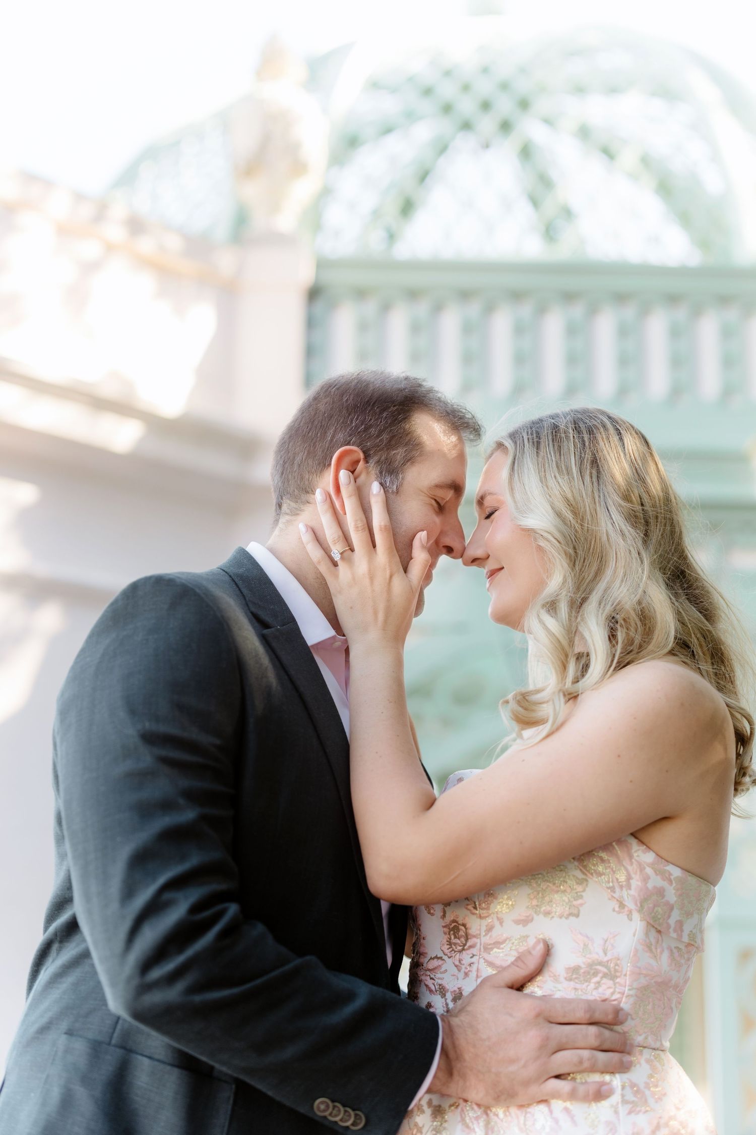 A romantic moment between a couple in formal attire sharing an intimate embrace in front of an ornate architectural backdrop.