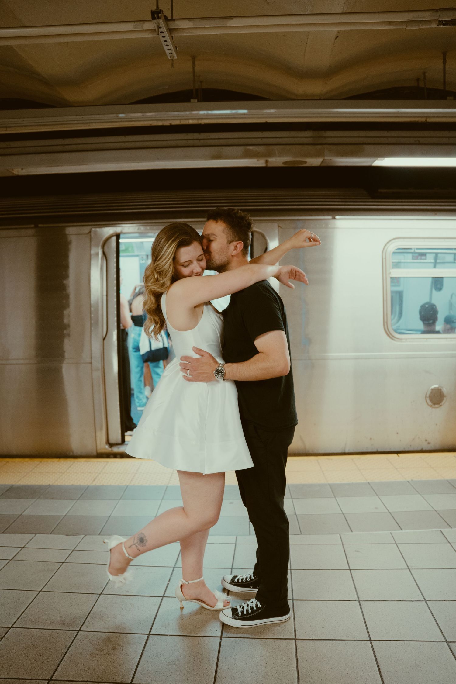 A romantic couple dances together in a subway station, creating an intimate moment on the tiled platform.