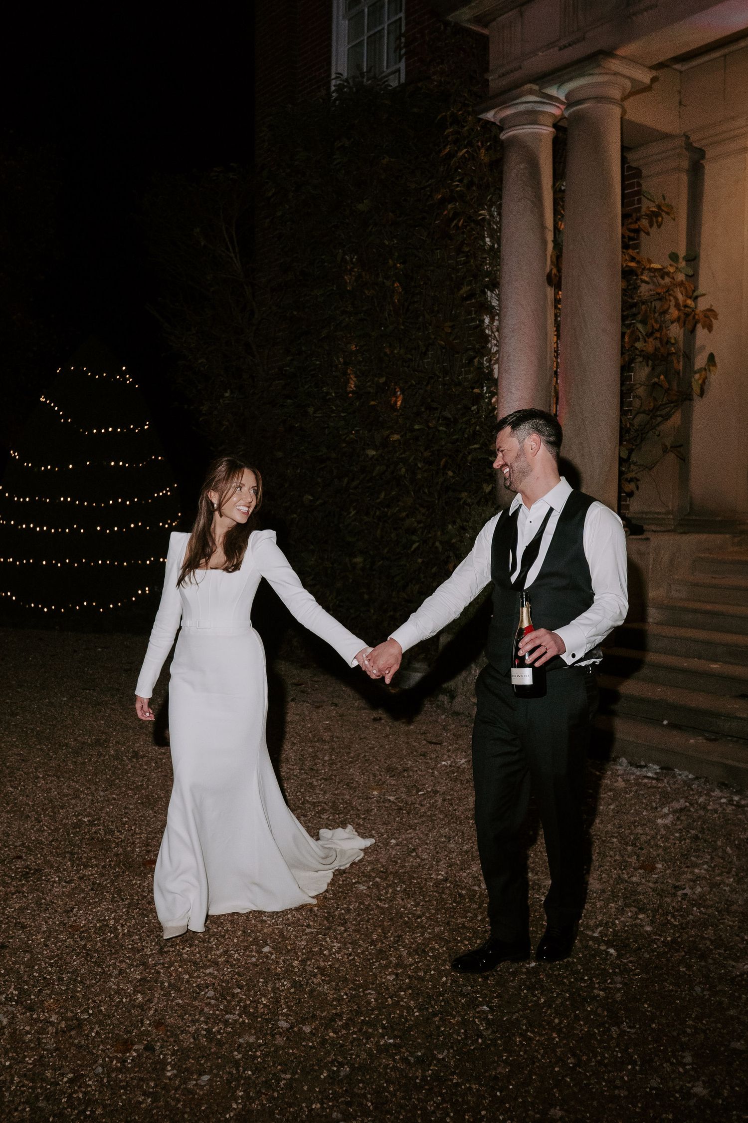 bride and groom holding hands walking away from Iscoyd park at night