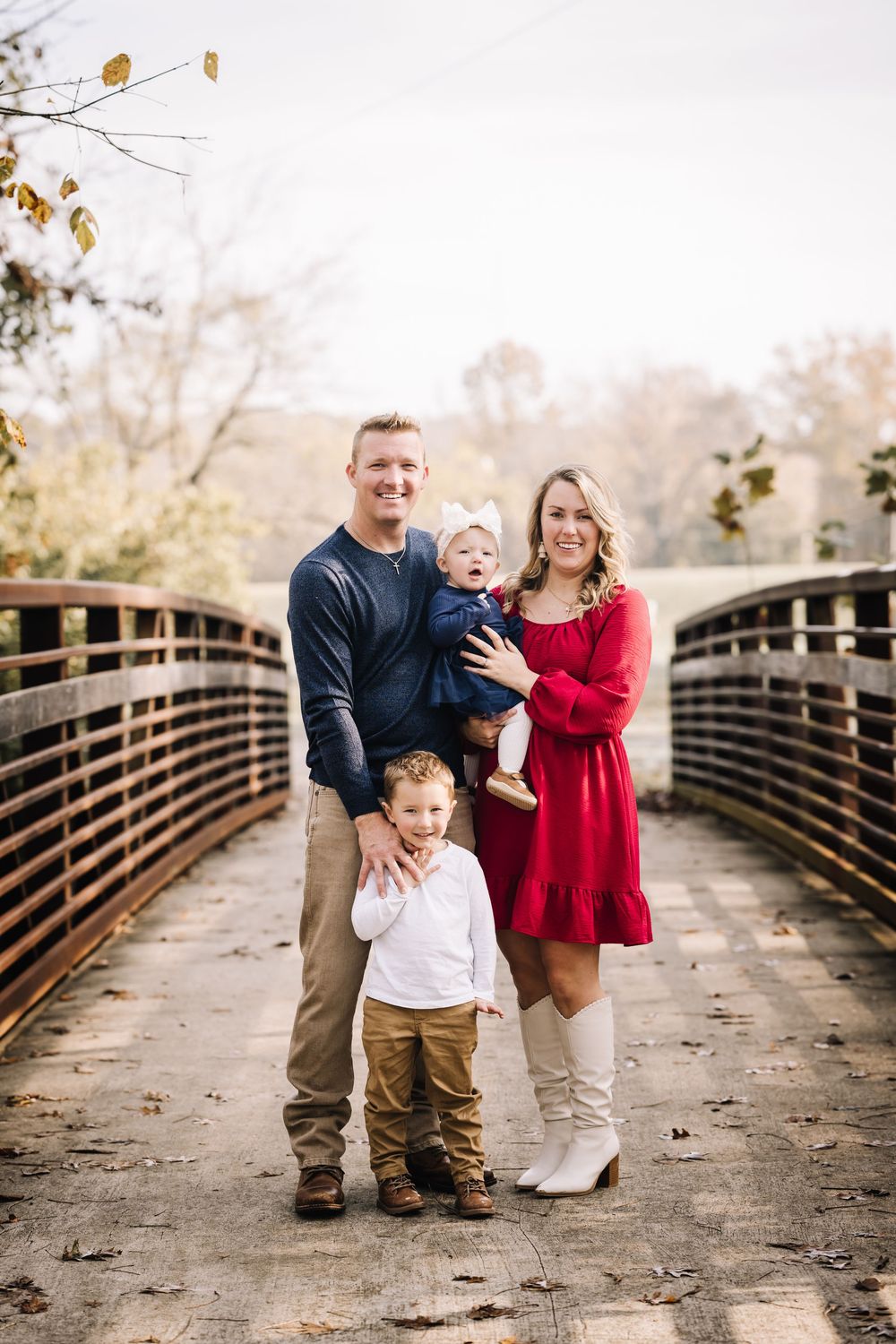 Family portrait on wooden bridge during autumn with fall foliage in background.