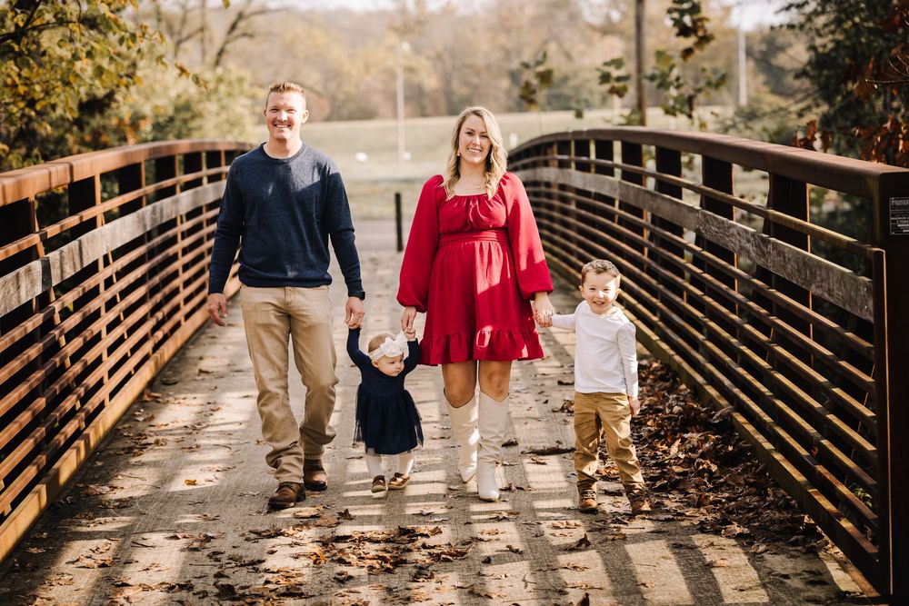 Family walking together on wooden bridge path during golden autumn afternoon.