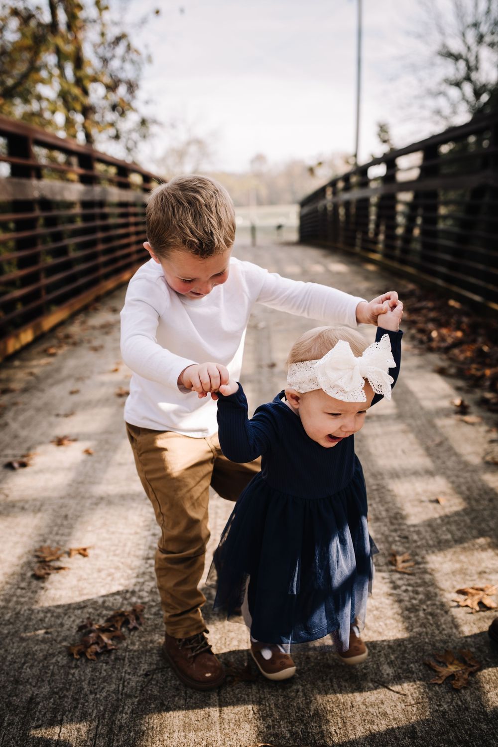 Two children playing and interacting on wooden bridge walkway in fall season.