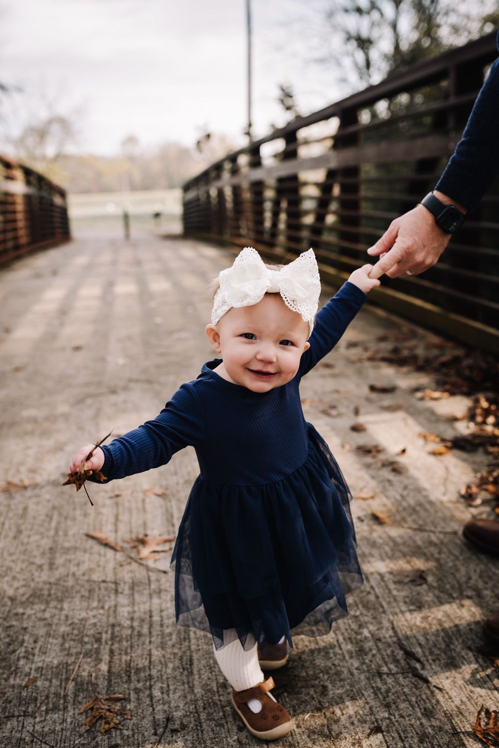 A small child in a navy tulle dress and white bow twirls on a wooden bridge.