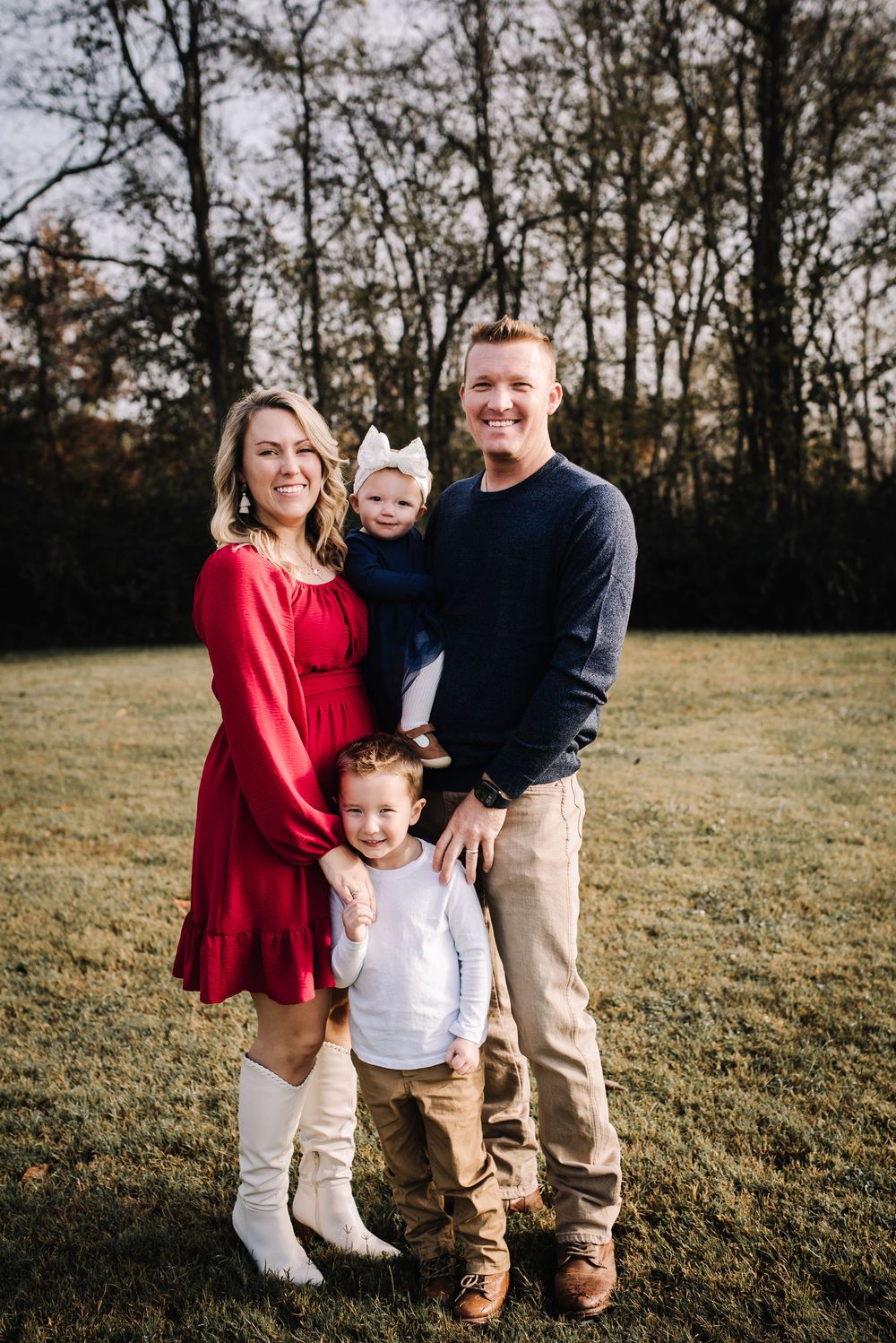 A family in coordinated red and khaki outfits poses together in a grassy field during golden hour.