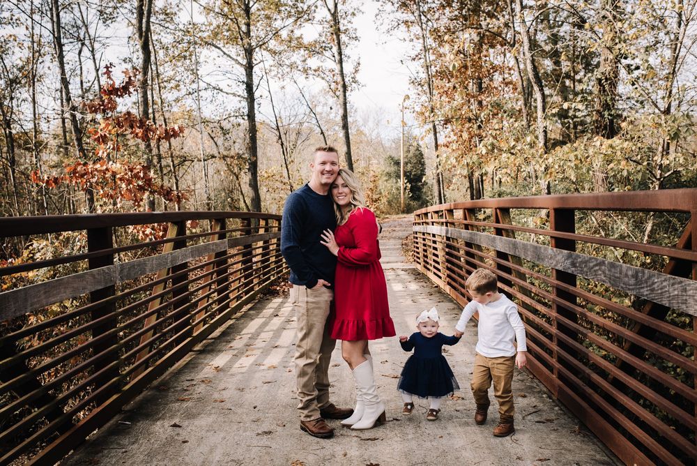 A family shares a warm embrace while standing on a wooden bridge during autumn.