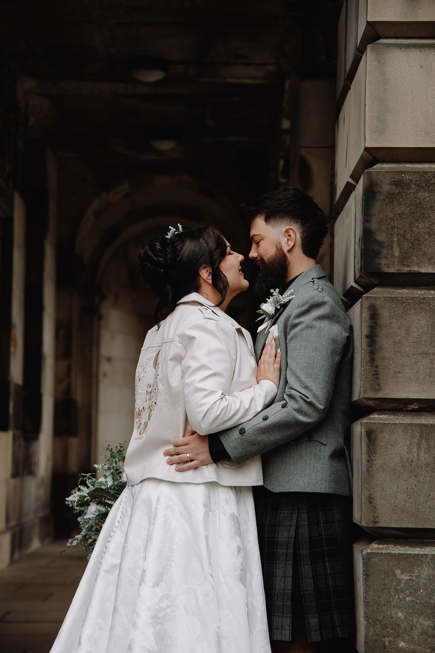 Intimate wedding portrait of couple embracing against stone architecture.