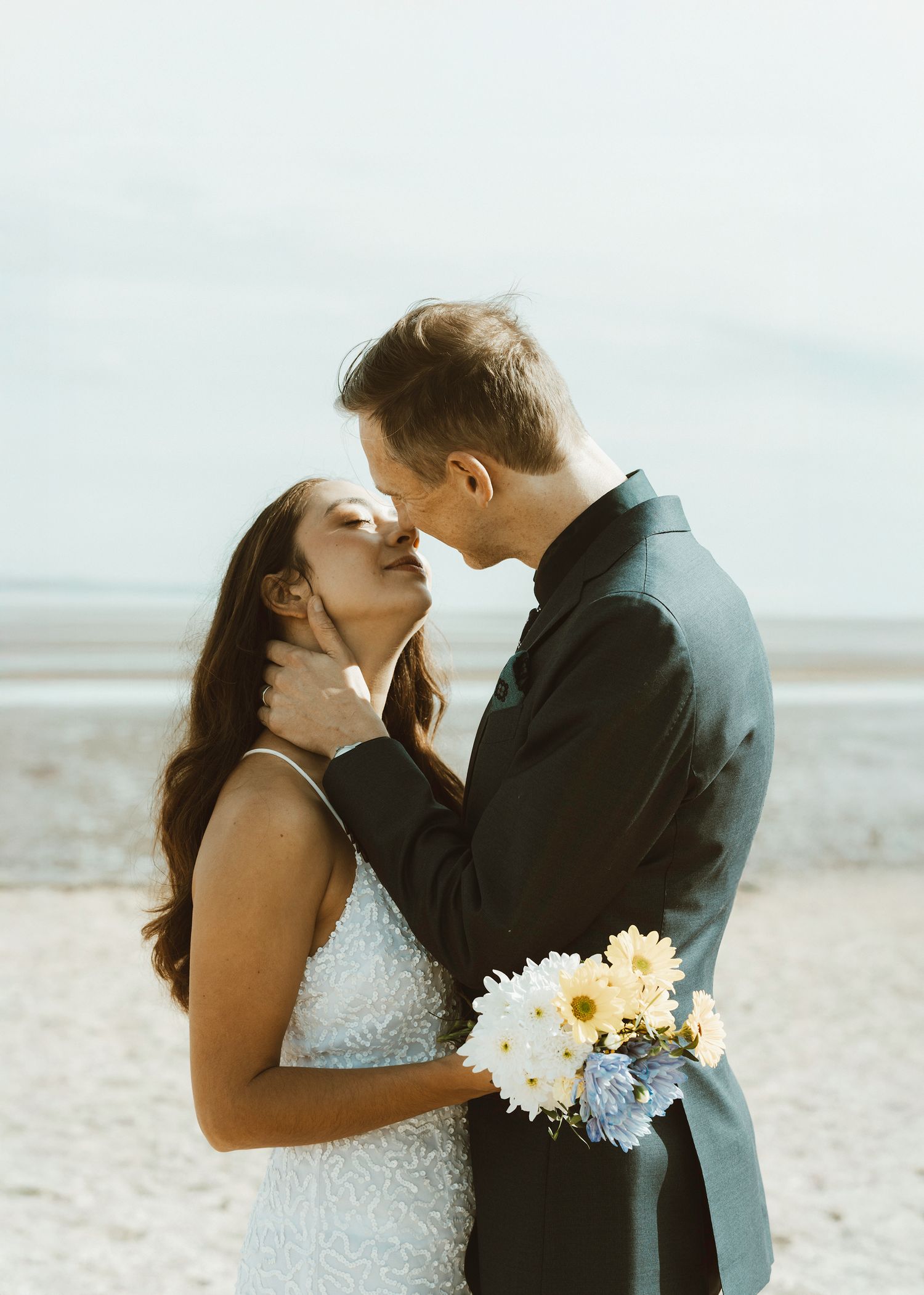 Romantic beach wedding portrait with white bouquet at sunset.