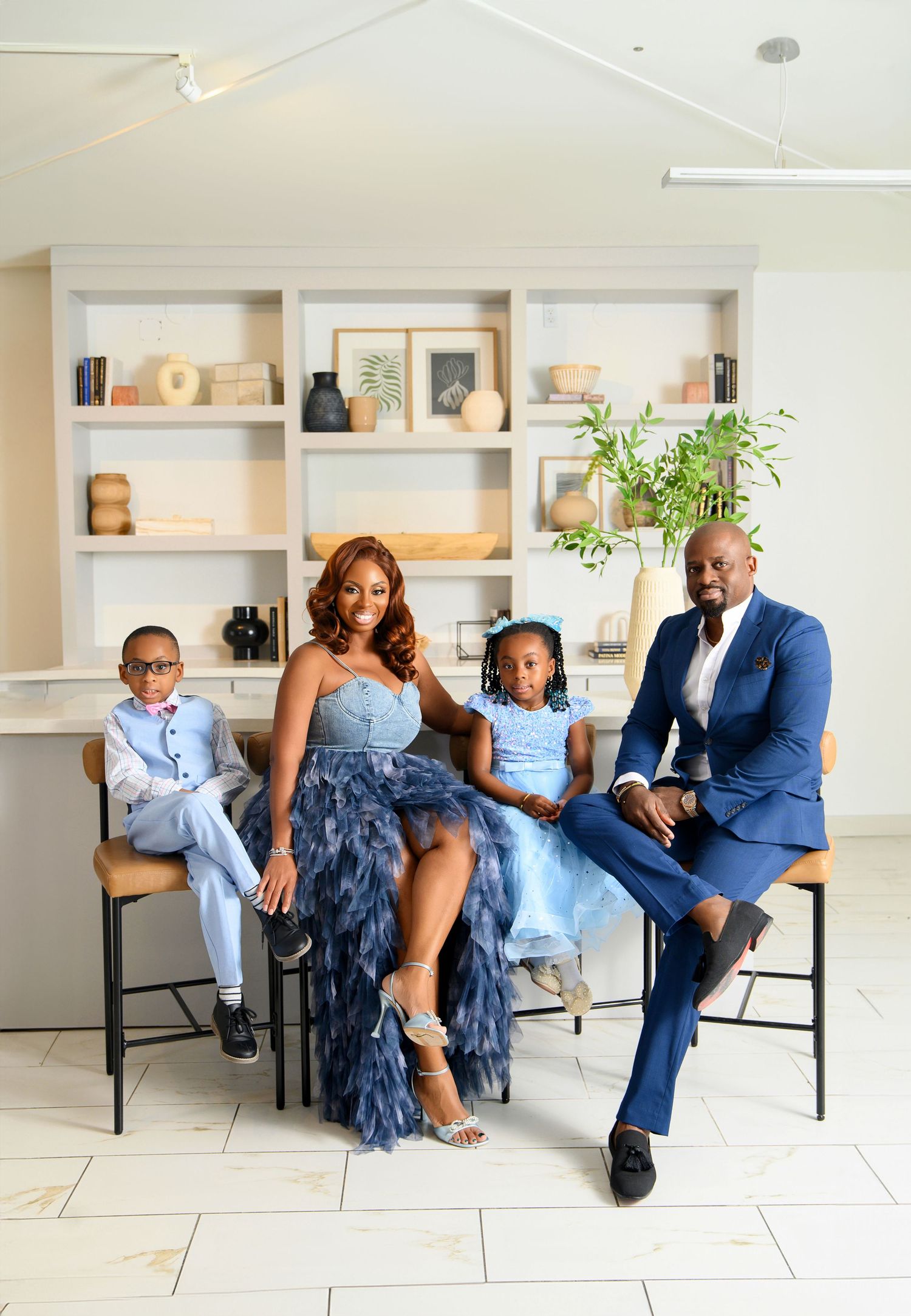 A group poses playfully on a hardwood floor against a white wall in formal attire.