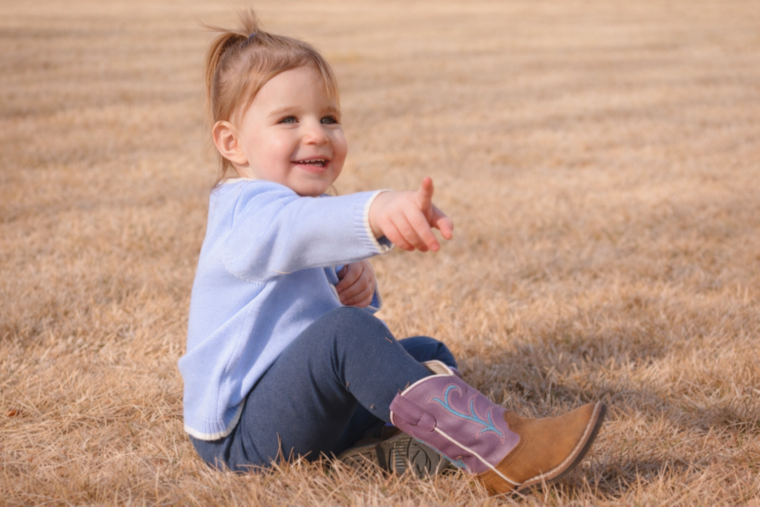 child sitting in field pointing happy