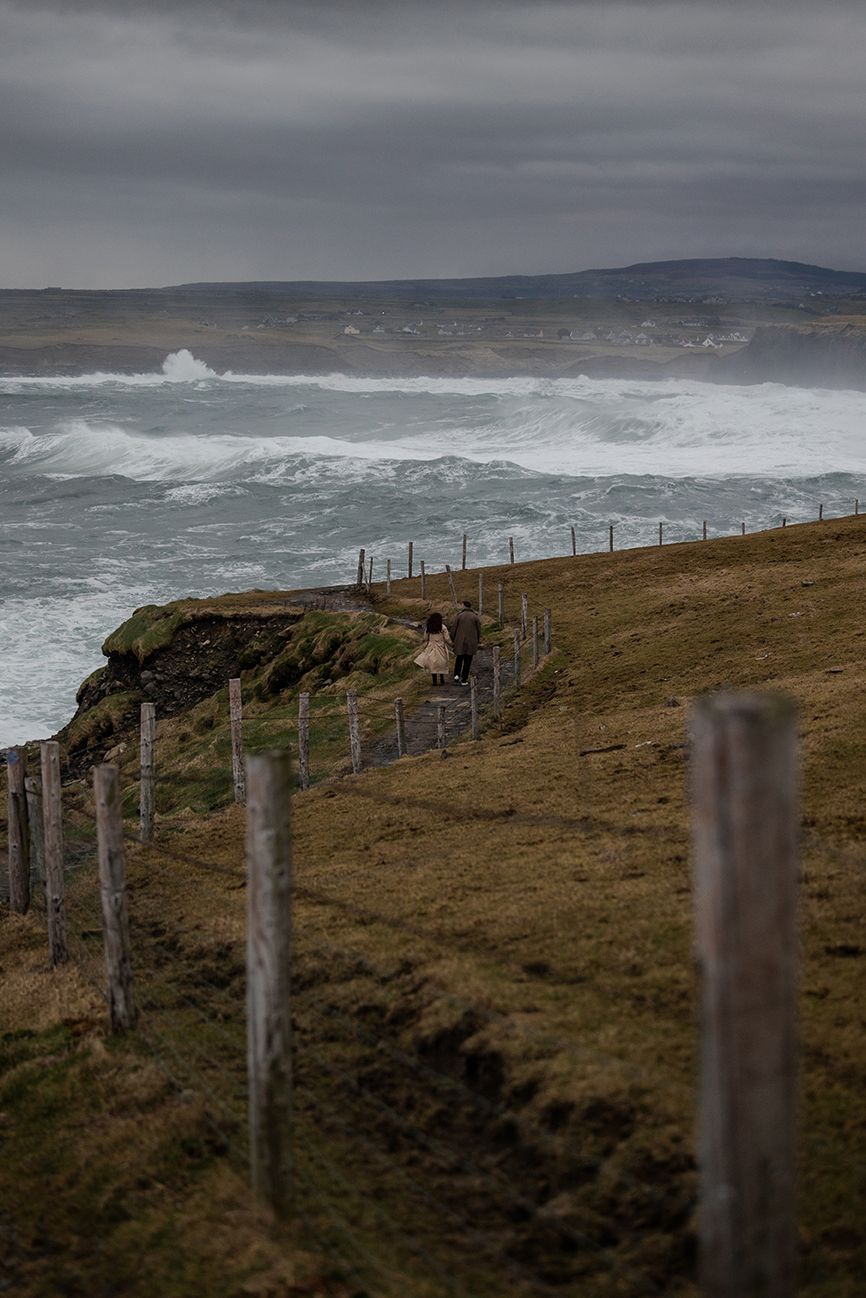 Couple exploring Doolin Cliff Walk as waves crash violently against limestone cliffs