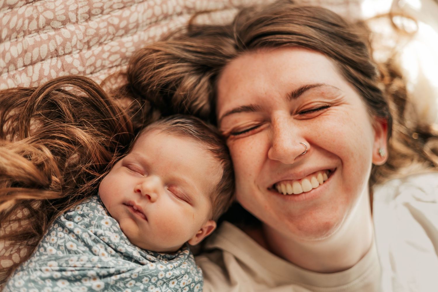 Smiling mother lying beside her sleeping newborn wrapped in a floral swaddle | Newborn Photos When You Don't Feel Like Yourself