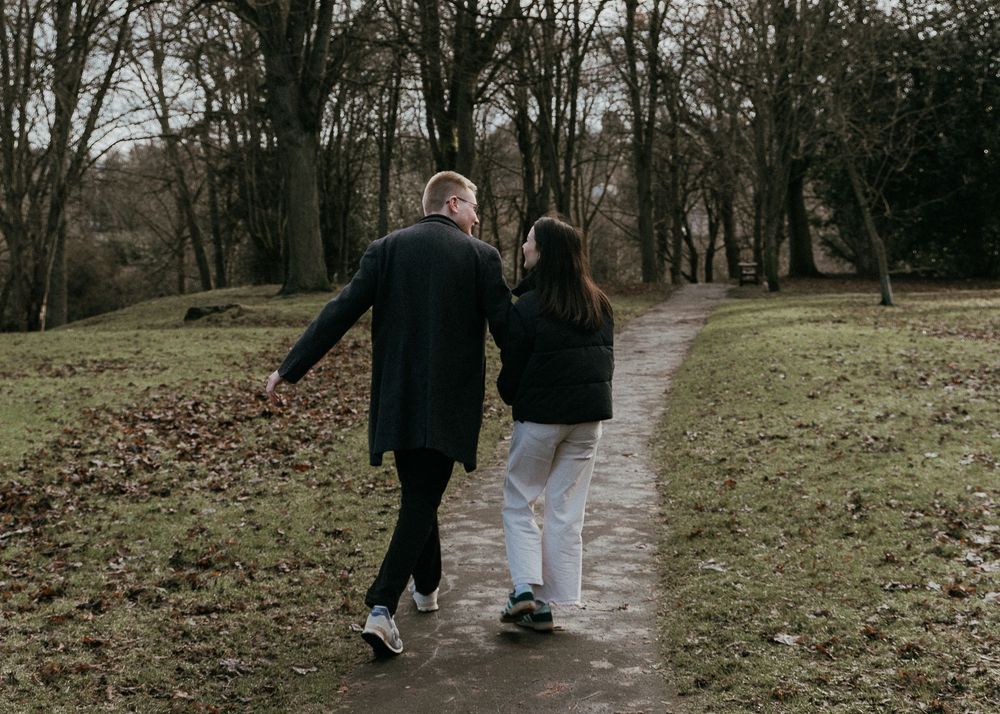 Couple walking hand in hand on a winding path through a bare winter park with leafless trees.