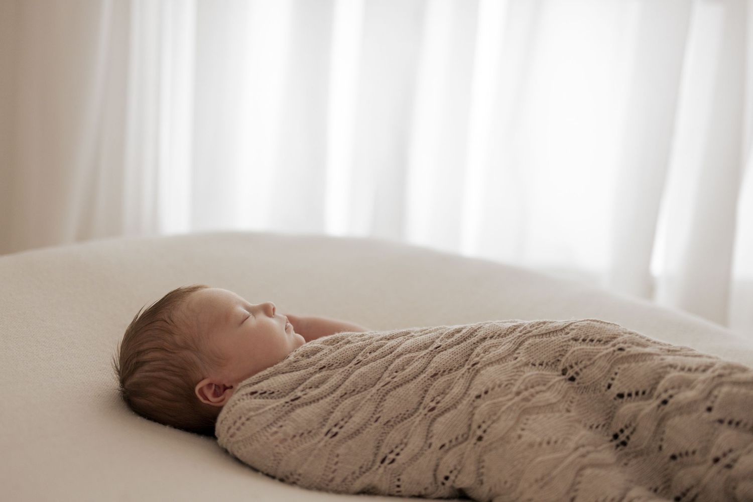 Baby sleeping soundly wrapped in textured knit blanket by window. Photography in Buckinghamshire.